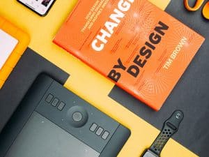 Design-Buch von Tim Brown auf Schreibtisch mit Grafiktablett und Smartwatch.