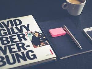 Arbeitsplatz mit Buch, Notizblock, Stift, Smartphone und Kaffeetasse.