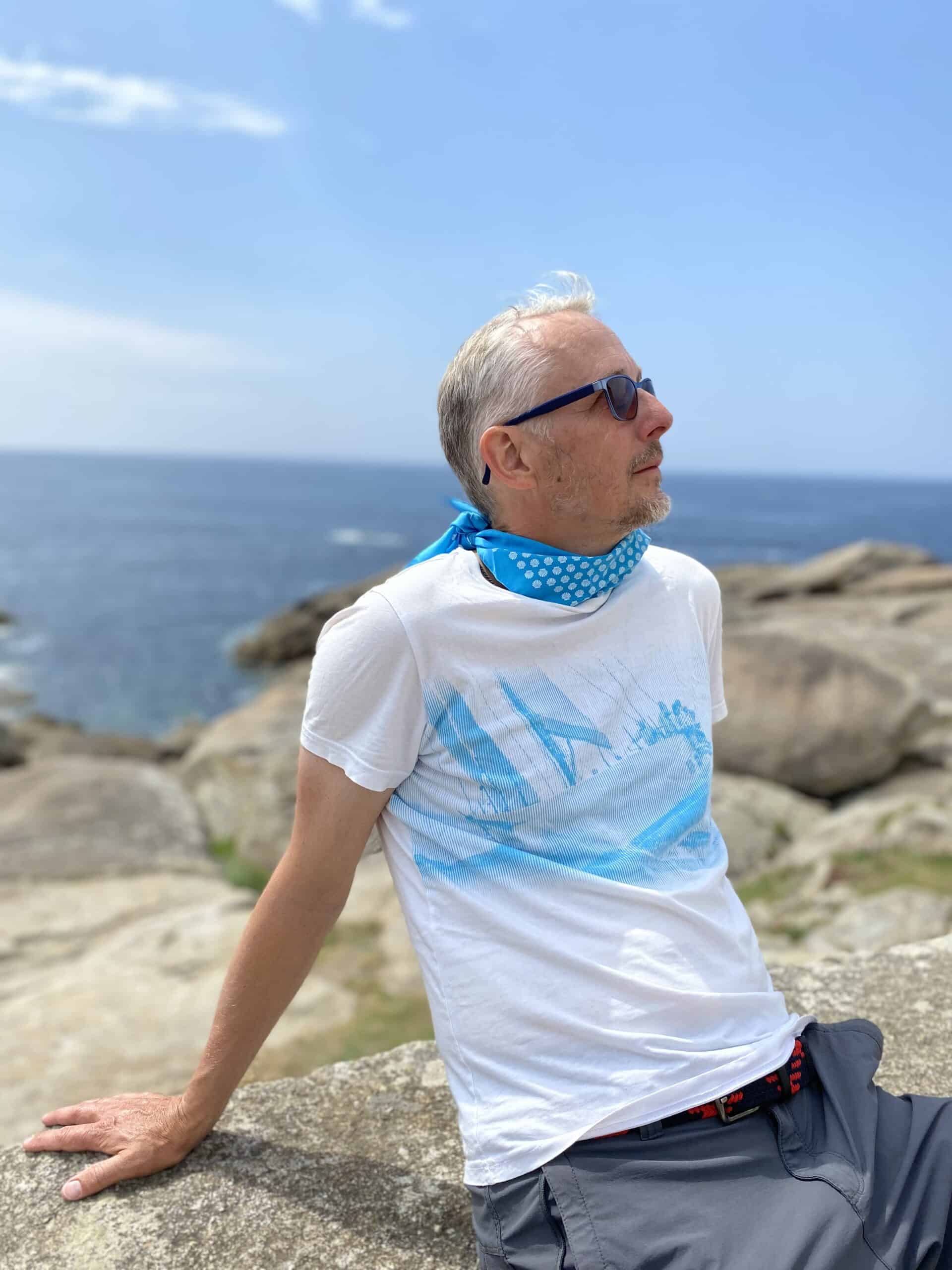 Tom Bohéme entspannt am Meer mit Sonnenbrille und blauer Halskette.